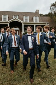 a group of men in suits and ties walking across a grass covered field next to a house