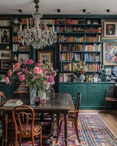 a dining room table with chairs and a chandelier in front of bookshelves