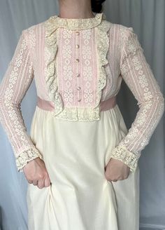 Details: maxi length; acetate lining with semi-sheer overlay; empire waist with pink ribbon trim (forms long bow in the back of the dress); blush bodice and sleeves with off-white lace overlay; faux button up front; ruffle lace trim around bodice; long sleeves with snap cuff closure; zip up closure in the back.  Damage: small stain on lace trim on left toward neckline and at base near waist trim; small tear toward bottom right hemline; stain along back right hemline.  Shoulders: 14.5 in // Bust: 34 in // Waist: 29 in // Hips (measured at acetate lining): 50+ in // Sleeves: 24 in // Overall Length: 59 in  Please note all inventory is pre-loved and sold as is. I will always do my absolute best to detail any and all damage in the description as well as photos. Formal Feminine Lace Dress With Ruffles, Feminine Formal Dress With Lace Patchwork, Feminine Formal Dress With Lace Bodice, Formal Feminine Dress With Lace Bodice, White Feminine Dress With Contrast Lace, Feminine Lace Dress With Fitted Bodice, Feminine Formal Dress With Lace Top, Pink Long Sleeve Dress With Lace Bodice, Elegant Daywear Dresses With Contrast Lace