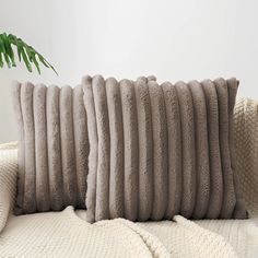 a close up of a pillow on a couch with a plant in the corner behind it