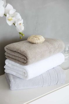 towels stacked on top of each other in front of a vase with white orchids