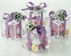 four small clear boxes with flowers and candles in them on a white surface, one has a purple ribbon tied around the top