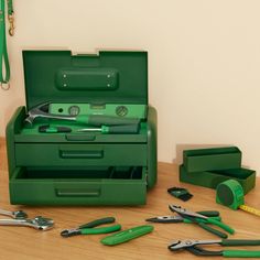 a green tool box with tools in it sitting on a wooden table next to other tools