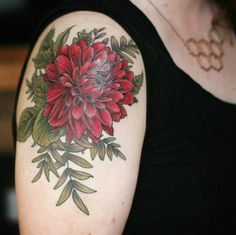 a woman's arm with a red flower and leaves tattoo on the left shoulder