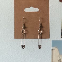 a pair of silver earrings sitting on top of a brown card next to a white wall