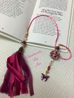 an open book with a pink tassel on top of it and a butterfly charm