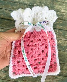 someone is holding up a crocheted bag with a ribbon around the top and bottom