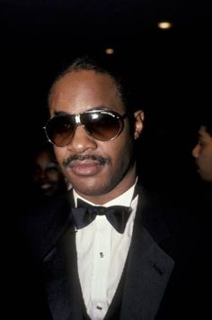 a man in a tuxedo wearing sunglasses and a bow tie at an event