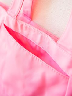 a pink tote bag hanging up against a wall with the bottom section partially open