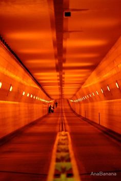 an empty tunnel with orange light coming in from the ceiling and lights on either side