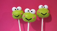 three green frog lollipops with googly eyes on pink background, closeup