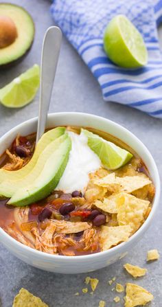 a white bowl filled with chicken tortilla soup and topped with avocado