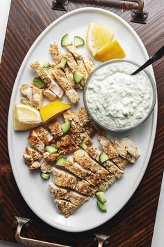 a white plate topped with chicken and cucumbers next to a bowl of yogurt