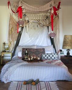 a canopy bed with pillows and candles on the floor in a room that has white walls