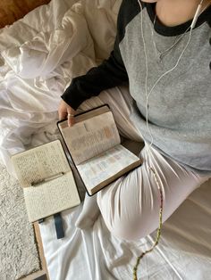 a person sitting on a bed with an open book and headphones in their ears