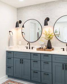 a bathroom with two round mirrors above the sinks and blue cabinetry on the wall