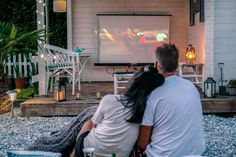 a man and woman sitting in front of a screen watching something on the back porch