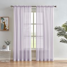 a living room with white curtains and a plant on the side of the window sill