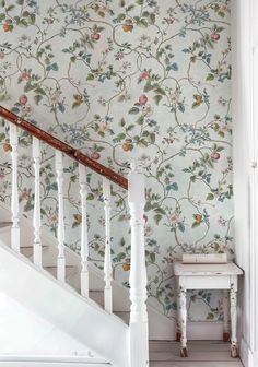 a white stair case next to a wall with flowers on it and a wooden banister