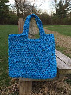 a blue crocheted bag sitting on top of a wooden bench in the grass