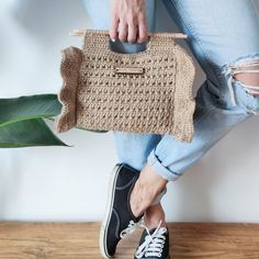 a woman is holding a crocheted purse on her legs and wearing black tennis shoes