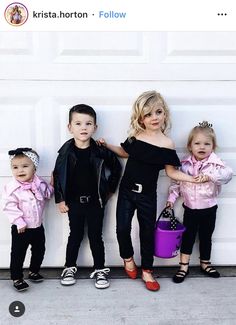 three children in black and pink outfits standing next to a garage door, one holding a purple bucket