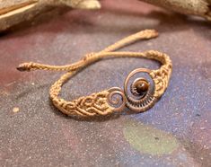 a rope bracelet with two spirals and a wooden bead on the end, sitting on top of a piece of wood