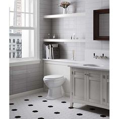 a white toilet sitting in a bathroom next to a sink under a window with black dots on the floor