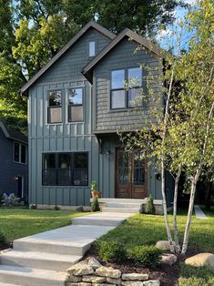 a gray house with steps leading up to the front door and trees on either side