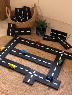 a toy car race track made out of cardboard with cars on it and two planters in the background