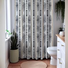 a white toilet sitting next to a shower curtain in a bathroom with a plant on top of it