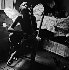 a black and white photo of a woman sitting in a chair with wings on her head