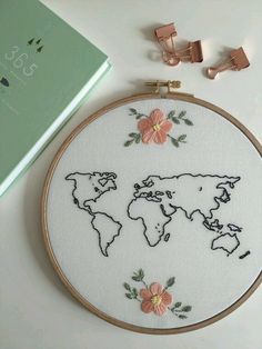 a cross stitch world map with pink flowers on it next to a pair of scissors