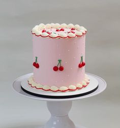 a pink cake with white frosting and cherries on the top is sitting on a pedestal