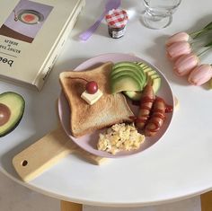 a white table topped with a plate of food next to flowers and an open book