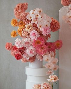 a tall white vase filled with lots of pink and orange flowers next to a wall