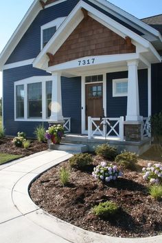 a blue house with white trim and flowers in the front yard