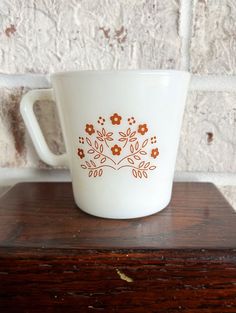 a coffee cup sitting on top of a wooden table next to a brick wall with flowers painted on it