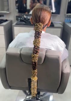 a woman sitting in a chair with a braid on it's head and gold beads hanging from her hair