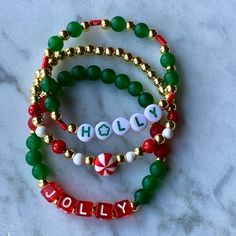 three christmas bracelets with the word holly and candy cane beads on marble counter top