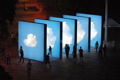 people walking around in front of large screens with clouds projected on them at night time