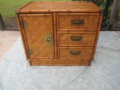 an old bamboo cabinet with brass handles on a tableclothed surface in front of a fence