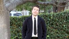 a man standing in front of a tree with his hands in his pockets and wearing a tie