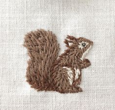 an embroidered squirrel sitting on top of a piece of cloth with white and brown thread