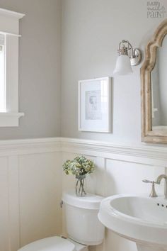 a white toilet sitting next to a sink in a bathroom under a mirror and framed pictures