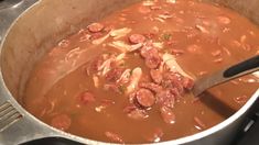 a pot filled with meat and vegetables on top of a stove next to a wooden spoon