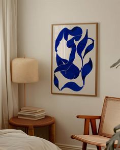 a painting hangs on the wall next to a chair and lamp in a room with white walls