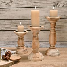 three candles sitting on top of a wooden table next to pine cones and other items