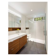 a bathroom with a walk in shower next to a white sink and wooden cabinetry