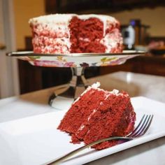 a slice of red velvet cake with white frosting on a plate next to a fork